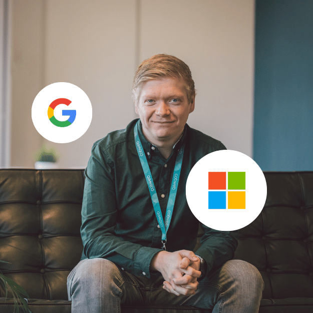 A blond man is sat on a corporate looking black sofa, with his hands together, smiling at the camera, ready to discuss a google workspace to Microsoft 365 Migration.